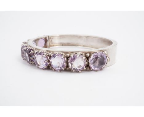 An amethyst and white metal hinged bangle, crown-set with nine circular (1 cm) stones, 58 x 51 mm internally