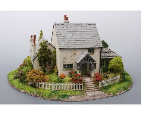 A hand-built scale model of a 19th Century Lakeland two-storey lime-washed cottage, situated on a verdant hill with rolling g
