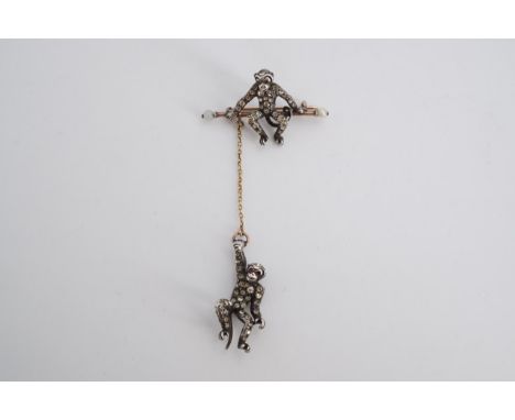 A late 19th / early 20th Century novelty paste-set yellow and white metal brooch in the form of a monkey sat on a bar with fa