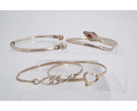 A white metal Celtic style torc bangle, a serpent bangle and two other silver bangles