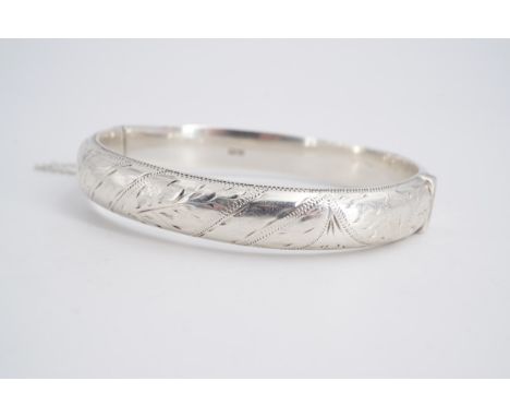 An early 1960s silver hinged bangle, of D-section and engraved in a pattern of spiral bands and foliage, 6.5 cm x 6 cm
