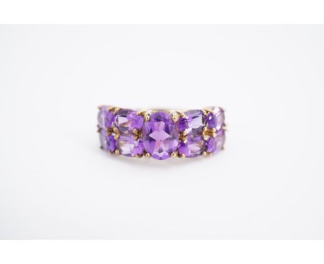 An amethyst ring, comprising a central oval stone claw-set between four pairs of smaller amethysts, on a yellow metal shank, 