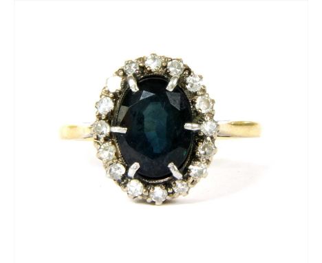A gold sapphire and diamond cluster ring, with an oval mixed cut sapphire, six claw set to a surround of eight cut diamonds, 