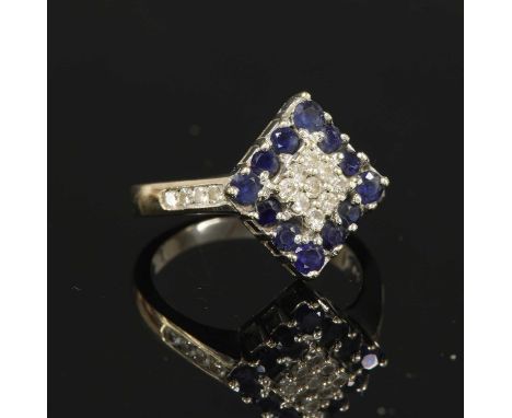 A white gold diamond and sapphire lozenge-shaped cluster ring, a central cluster of nine brilliant cut diamonds, with a borde