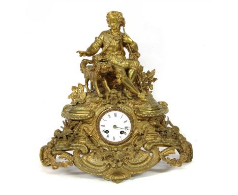 A gilt metal mantel clock, the seated figure of a young man in 18th century attire beside a dog carrying a basket of flowers 