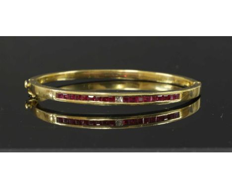A gold diamond and ruby set flat section hinged bangle, a princess cut diamond with a row of square step cut rubies at each s