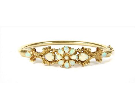 A 9ct gold opal bangle, a round cabochon opal to a border of pear shaped cabochon opals, claw set to form a flowerhead cluste