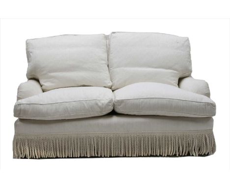 A cream upholstered two seater sofa, with a tasselled fringe, 152cm wide, 100cm deep, 85cm high
