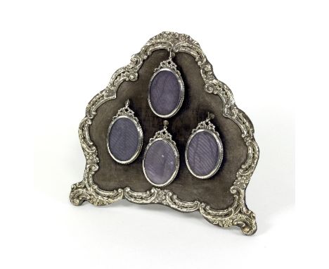Four oval silver frames, HM, Birmingham 1900, with ribbon-tie surmounts all hung on a cartouche shaped easel frame with scrol