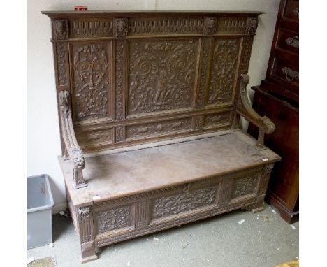 An early 19th century oak Monk's bench, carved top rail with cherub masks, back carved with floral, scroll and cherub decorat
