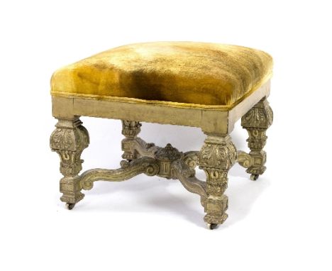 A carved gilt gesso stool with leaf and scroll carved legs and an X stretcher support on brass castors with mustard velvet up