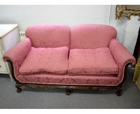 An upholstered two-seater sofa with carved frame, on ball and claw feet