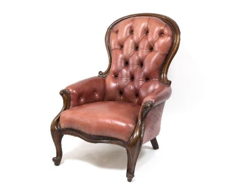 A Victorian walnut framed fireside chair with faded red leather button back upholstery