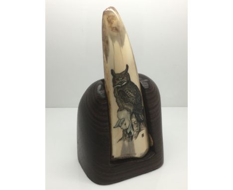 An Eskimo fossil walrus tusk scrimshaw depicting a rabbit and an owl, raised on a hardwood stand, approx 16cm.