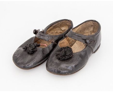 A pair of black leather children's shoes with a strap and button fastening, rosette detail on the front, (1916 - 1918)