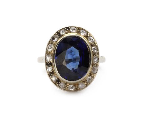 A white gold synthetic sapphire and diamond cluster ring, an oval mixed cut synthetic sapphire, rub set, to border of rose cu