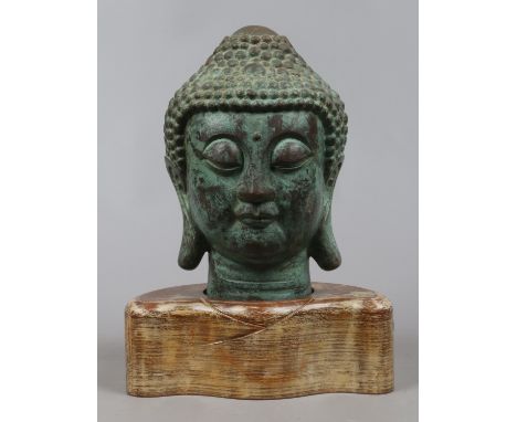 A Chinese bronze of a Buddha head raised on wooden plinth.