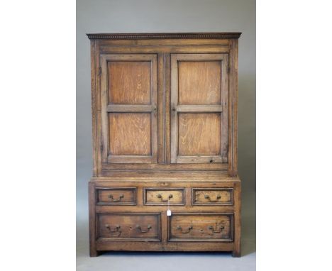 A JOINED OAK CLOTHES CUPBOARD, early/mid 18th century, the dentil moulded cornice over a pair of twin panelled doors enclosin