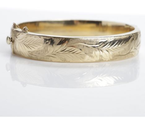 NINE CARAT GOLD HINGED BANGLE
of oval form, with engraved foliate motifs, with safety chain, 22g