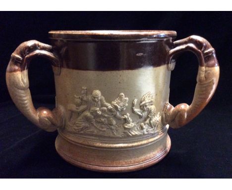 A LARGE AND RARE VICTORIAN SALT GLAZE POTTERY TYGG  Mounted with three handles moulded as greyhounds, the panels having appli