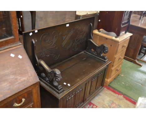 An oak Monk's bench by L. Marcus Ltd. tilt top, stylized lion arms, hinged cover to seat, linenfold panelling to front.