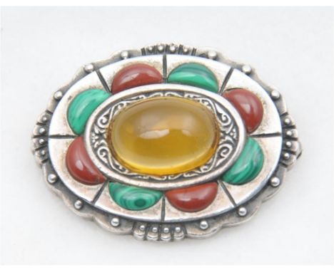 An early 20th century Arts & Crafts style brooch, of circular form with a central oval cabochon amber coloured stone, within 