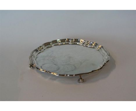 A George V hallmarked silver circular salver having a cast scalloped edge, raised on three scrolling feet, made by Harrison B