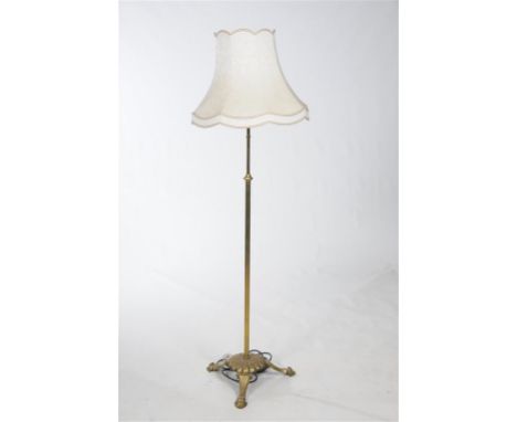 An Edwardian brass standard lamp with a cylindrical column, lobed circular plinth, triform down swept leafy feet with a shade