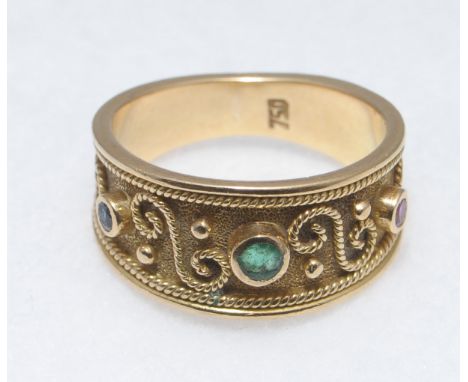 A stamped 750 multi gem set dress ring, the wide tapering band with applied wirework having a round cut ruby, emerald and sap