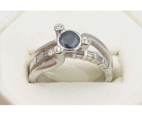 A contemporary sapphire and diamond set dress ring, the central round cut sapphire collet set to a border of three tiny diamo
