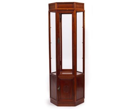 AN ORIENTAL HARDWOOD HEXAGONAL FLOOR STANDING DISPLAY CABINET with glazed sides, the panel base with single cupboard door, 58