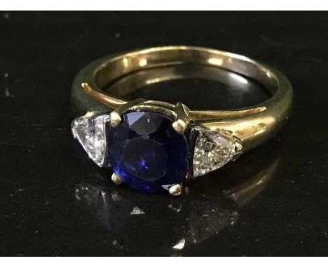 An 18ct gold sapphire and diamond ring, the cushion-cut sapphire within a four claw setting flanked by two trilliant-cut diam