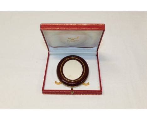 Le Must de Cartier gilt metal and red enamel oval photograph frame with easel back and cabochon blue stone studs, in original