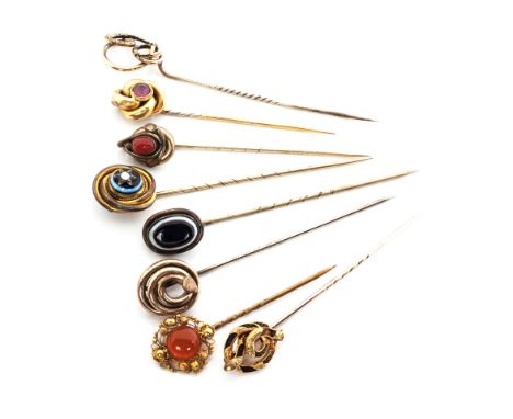 A COLLECTION OF EIGHT GOLD STICK PINS one surmounted with a stylised coiled snake, the others surmounted with semi-precious s