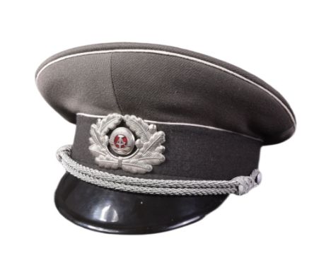 A Cold War period East German Army / DDR Officers peaked uniform cap. The grey cap with white piping and a central badge depi