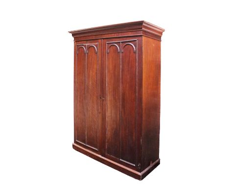 A 19th Century mahogany two door Wardrobe, the shaped cornice above two panel doors with moulded arch motifs on a plinth base