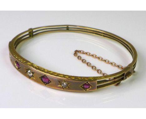 A Victorian 9ct gold, diamond and ruby bangle, set with four rubies and three diamonds, each within a starburst setting on th