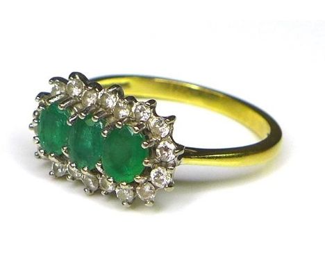 An 18ct gold, emerald and diamond ring, the three oval cut emeralds each of 5 by 4mm surrounded by 18 diamonds of approximate