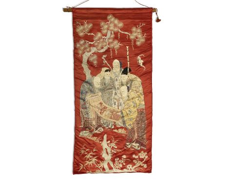 A CHINESE CORAL GROUND SILK PANEL, C.1900Woven with a group of immortals standing under a pine tree, unfurling a scroll paint