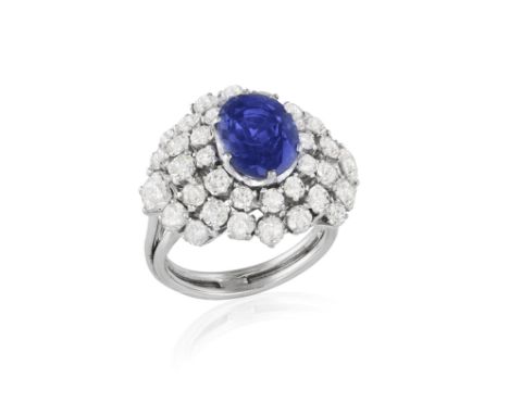 A SAPPHIRE AND DIAMOND CLUSTER RING, ITALIAN, CIRCA 1960, set with an oval-shaped sapphire at the centre within a six-claw se