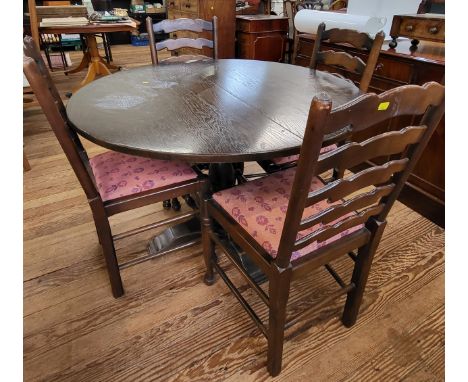 A circular dining table and four ladder-back dining chairs with red upholstery. Table measures 73cm x 112cm