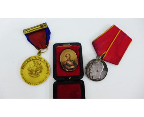 A white metal Russian medal with red ribbon with yellow edges, a gilt metal Republique D'Haiti medal with red ribbon with blu