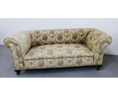 An early 20th century drop end sofa with a floral tapestry upholstery on mahogany supports and brass caps and castors, 183 x 