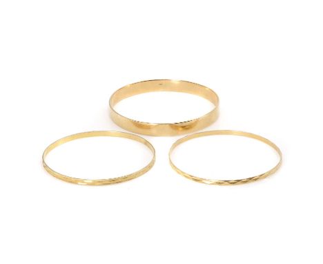 A group of three gold bangles, a round bangle,with a flat profile, 8mm width, internal diameter 69mm, stamped 18CT, a thin ro
