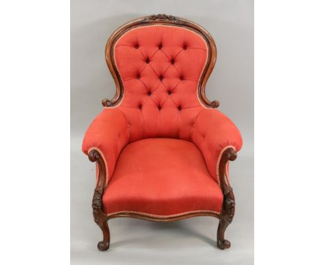 A Victorian foliate carved mahogany frame armchair, button down upholstered in red material, on cabriole legs.

