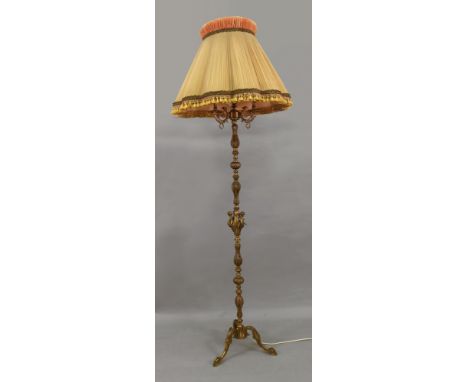 An ornate gilt metal three light standard lamp, cast with putti and leaves, on tripod base, 195cm high, with tasselled shade.