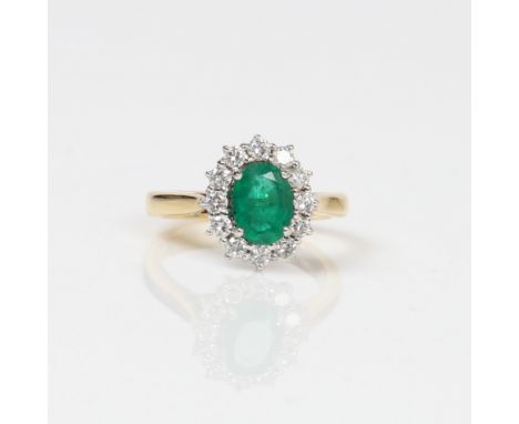 18CT GOLD EMERALD AND DIAMOND CLUSTER RING. One oval mixed cut emerald approx. 1ct. Surrounded with round brilliant cut diamo
