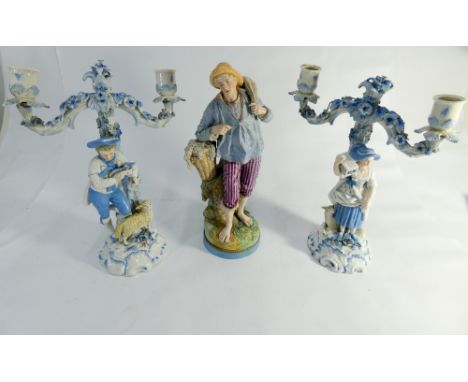 A continental coloured bisque ware figurine of a fisherman together with a pair of pastoral figural candlesticks in pale blue