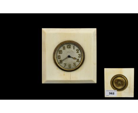 An Early 20th Century Travel Clock Square form clock set in cream cellulose, brass mount with cream ceramic dial and gold ton
