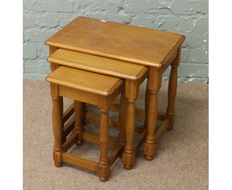 A nest of three light oak occasional tables raised on turned legs.